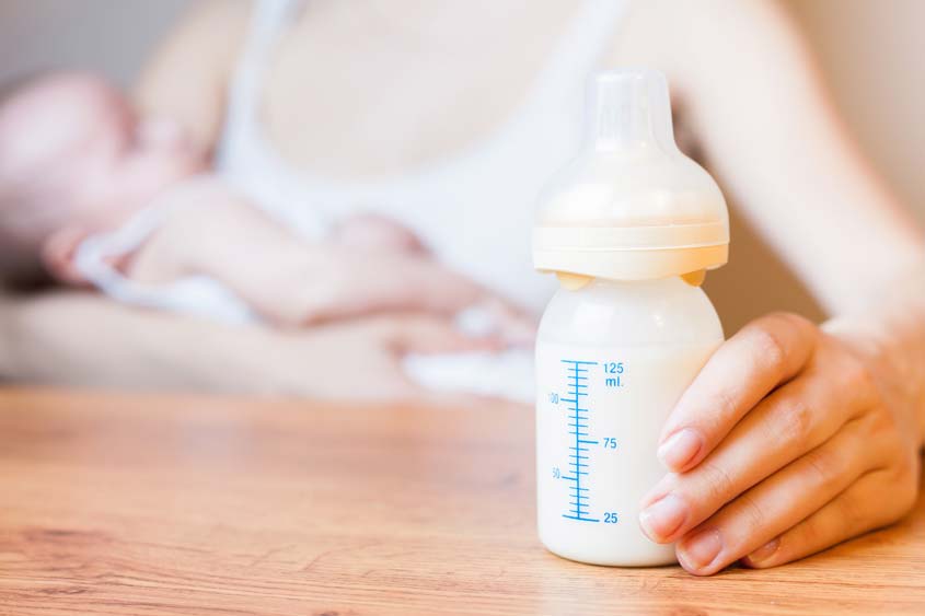 Mulher oferecendo leite materno de mamadeira ao bebe.