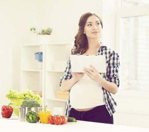 Mulher grávida na cozinha segurando uma lista de papel e refletindo
