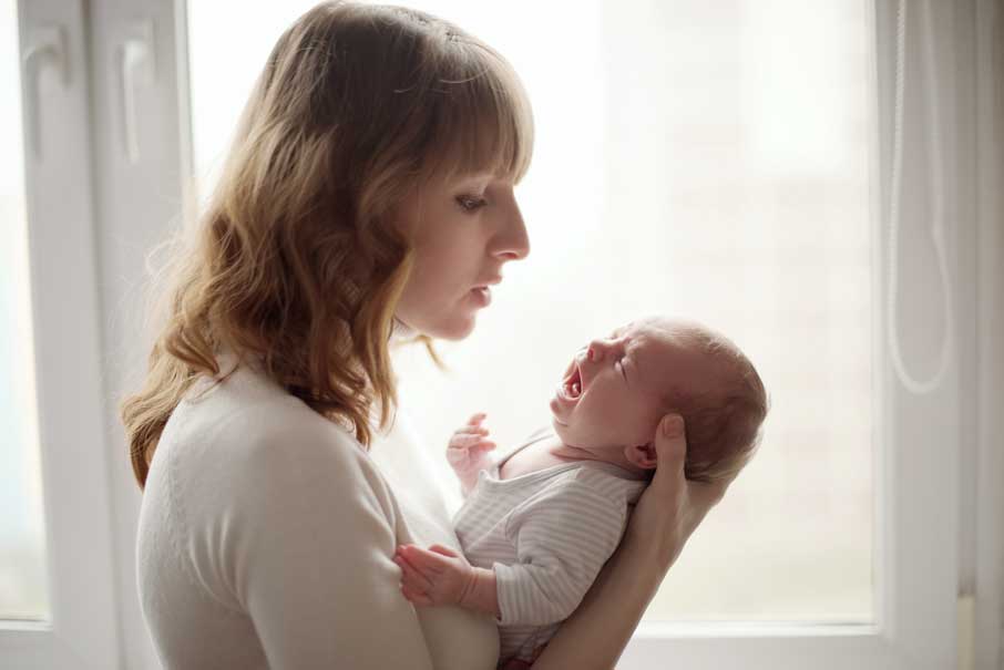 Mulher jovem segurando bebê chorando de cólica