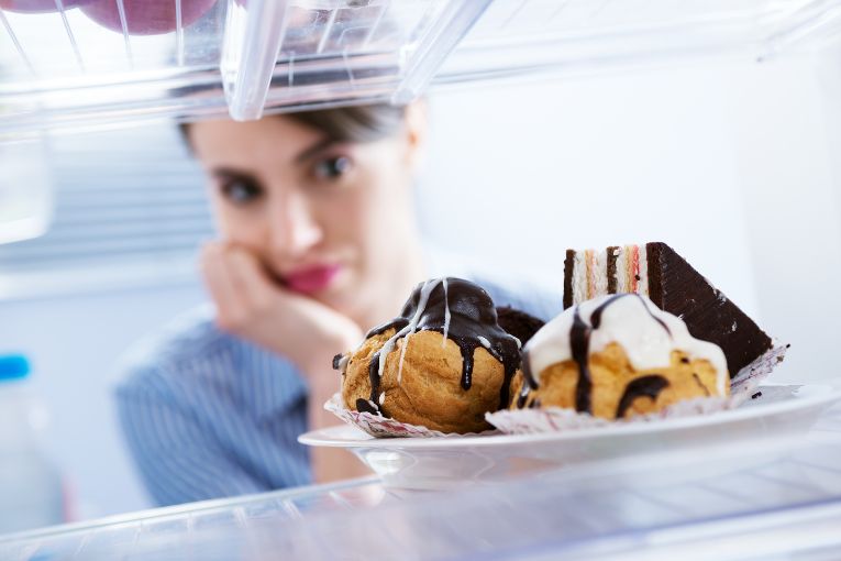 mulher olhando para doces na geladeira, indício de comportamento que atrapalha a prevenção da diabetes gestacional